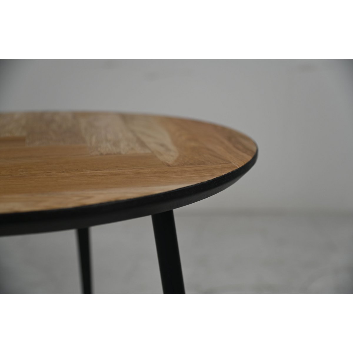 Ronde vimba salontafel van eikenhout met drie zwarte metalen poten en zwarte swiss edge randafwerking houtpatroon